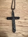 Détail macro du collier croix en acier inoxydable noir avec texture martelée sur bois - Incrustation d'acier inoxydable noir