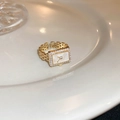 Nahaufnahme eines goldenen Rings im Uhrenstil mit Zirkonia auf Keramiktablett - Einstellbar Offen / Gold