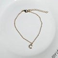 Detalle de una pulsera dorada con colgante letra C y circonitas en un plato blanco - Letra C