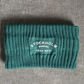 Makro-Detail des dunkelgrünen Strickstirnbands mit weiß geprägtem Stockholm-Sweden-Text - Dunkelgrün