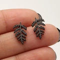 Macro shot of minimalist black leaf stud earrings held on fingertips for size reference - Leaf / Black
