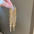 Detailed view of long gold tassel earrings with metallic leaf charms held by hand - Leaf Tassel Ear Buckle Style / Gold