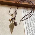 Gros plan du pendentif plume et étoile en bronze avec cordon brun et perles en bois - Style Grande Plume Dorée (HN9210)