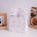 Detailed view of white paper gift bag with grey bow patterns and cute seal sticker - Silver