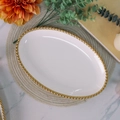 Vue détaillée d'une assiette en céramique blanche avec bord doré perlé sur un set - Plat Ovale à Bordure Perlée Dorée 14 Pouces