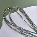 Close-up of 2mm square hematite beads in metallic blue and gold in a white shell bowl - Green