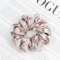 Minimalist champagne gold satin scrunchie with soft pleated texture on a magazine - Nude