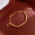 Detail view of gold titanium steel bracelet with clover charm on silk background - Gold