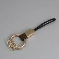 Porte-clés doré avec lanière en cuir marron et boucle en cordon tressé noir sur gris - Marron + Or