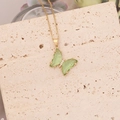 Gros plan d'un pendentif papillon avec ailes vertes et chaîne dorée sur travertin naturel - Vert