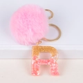 Macro shot of resin letter R keychain with pink pompom and gold foil flakes detail - Letter R