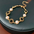 Détail du bracelet doré avec perles roses et gemmes noires sur fond de cuir vert foncé - Doré