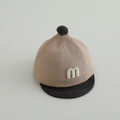 Dettaglio del cappellino bicolore per neonati con toppa M e pompon sulla punta - 48cm (Neonato) / Cachi Nero
