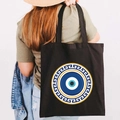 Black canvas tote bag with Greek Evil Eye print shown on a model's shoulder - Design I-Greek Key Eye-Black
