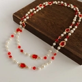 Détail d'un collier de perles vintage à deux rangs avec pierre rouge sur bois et fond blanc - Rouge