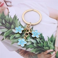 Primer plano de llavero dorado con tres dijes de flores de esmalte azul claro y centro de oro - Azul