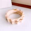 Close-up of a wide acrylic bangle featuring a scalloped gear edge and marble texture - Beige