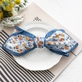 Primer plano de un lazo de satén azul con flores sobre un plato blanco decorativo - Azul Floral