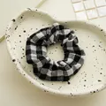 Dettaglio di un elastico per capelli a scacchi bianco e nero con texture a pieghe su vassoio - Griglia Nera