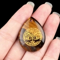 Tiger Eye teardrop pendant with Tree of Life engraving held in hand on black background - Tiger's Eye