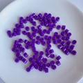 Macro detail of purple cylindrical acrylic spacer beads scattered on a white ceramic plate - 3# Purple