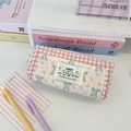 Close-up van roze geblokte etui met schattig borduursel en blauwe strik op bureau - Zachtroze Geruit