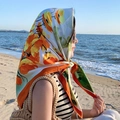 Square silk scarf with orange floral pattern worn as a headscarf at the beach - Verbena-White Orange Border