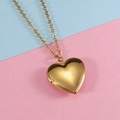 Detailed view of a gold heart locket necklace on a pink and blue two-tone background - Gold
