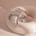 Detailopname van een brede zilveren geometrische ring op een beige golvende houder - Onregelmatige Golf (HB3374) / Zilver