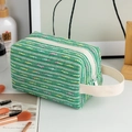 Close-up of green tweed makeup bag showing woven texture, white zipper and side handle - Light Green