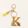 Detalle de llavero de acrílico letra K con diseño de abeja y borla de color amarillo - Letra K
