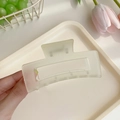 Matte beige large hair claw clip for thick hair shown in a hand over a tray - Transparent Yellow