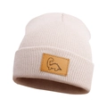 Close-up of beige knit beanie with a brown leather patch featuring a dinosaur graphic - Beige