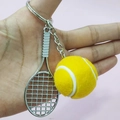 Detail shot of a mini tennis racket and ball keychain accessory held in hand - 3.8cm Ball / Yellow