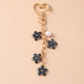 Close-up of golden heart clasp with black flower charms and a white pearl on the keychain - Heart Ring / Black
