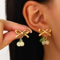 Detail of gold bow cherry earrings with white beads and green leaves on ear - 18K Gold Plated White Cherry Stud Earrings (7710)