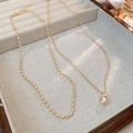 Detail of double-layer gold necklace with irregular pearl pendant in a wooden tray - Gold