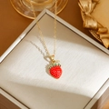 Close-up of strawberry pendant necklace with red enamel and green crystal details - Gold Strawberry