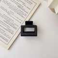 Detailed view of a matte black square hair claw clip placed on an open English book page - Matte Black