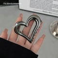 Metallic heart-shaped hair claw clip in dark grey finish held by a model - Heart Hollow / Black