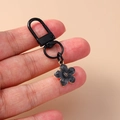 Macro shot of black enamel five-petal flower keychain charm with gold metal details - Black Flower