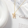Close-up of gold letter H pendant necklace with zircon flower on magazine page - Letter H