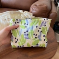 Détail de pochette en tissu à fleurs avec texture plissée et fermeture zippée - Plis Irréguliers Vert Violet sur Fond Blanc