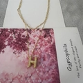 Collier double couche doré avec pendentif lettre H texturé sur une carte papier - Lettre H