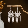 Detailed view of silver ethnic leaf tassel earrings hanging on a natural wooden branch - Silver Vintage Floral Carved Tassel Style (E2873-18)