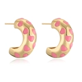 Macro view of C-shaped gold hoop earrings with pink enamel heart patterns - Pink