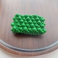 Detailed top view of a handmade green beaded coin purse on a minimalist wooden tray - Green