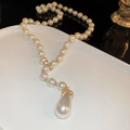 Dettaglio di una collana di perle a Y con ciondolo a goccia dorata su un piatto bianco - Bianco