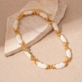 Détail d'un collier vintage en émail avec maillons X dorés sur une surface en pierre - Collier Blanc