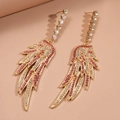 Detalle de pendientes de ala dorados con cristales rosas sobre un fondo beige suave - Dorado (Pasador de pendientes de plata de ley 925)